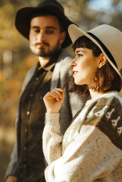 Lovely hipster couple looking at each other. Couple wearing beautiful hats and sweaters. Lifestyle, happy couple of two play on a sunny day in the park. The concept of youth, love and lifestyle. Sunset in autumn  - Foto, Imagem