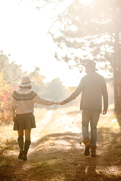 Lovely hipster couple looking at each other. Couple wearing beautiful hats and sweaters. Lifestyle, happy couple of two play on a sunny day in the park. The concept of youth, love and lifestyle. Sunset in autumn  - Фото, изображение