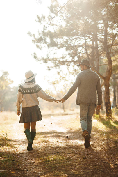 Lovely hipster couple looking at each other. Couple wearing beautiful hats and sweaters. Lifestyle, happy couple of two play on a sunny day in the park. The concept of youth, love and lifestyle. Sunset in autumn  - Foto, Imagem