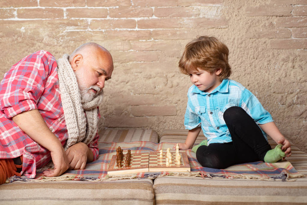 Little boy playing chess with his Grandfather. Chess piece. Senior man thinking about his next move in a game of chess. - Photo, Image