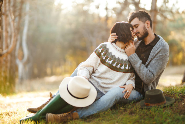 Lovely hipster couple looking at each other. Couple wearing beautiful hats and sweaters. Lifestyle, happy couple of two play on a sunny day in the park. The concept of youth, love and lifestyle. Sunset in autumn  - Fotó, kép