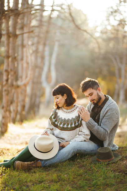 Lovely hipster couple looking at each other. Couple wearing beautiful hats and sweaters. Lifestyle, happy couple of two play on a sunny day in the park. The concept of youth, love and lifestyle. Sunset in autumn  - Zdjęcie, obraz