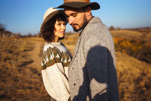 Lovely hipster couple looking at each other. Couple wearing beautiful hats and sweaters. Lifestyle, happy couple of two play on a sunny day in the park. The concept of youth, love and lifestyle. Sunset in autumn  - Фото, изображение