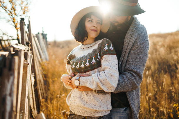 Lovely hipster couple looking at each other. Couple wearing beautiful hats and sweaters. Lifestyle, happy couple of two play on a sunny day in the park. The concept of youth, love and lifestyle. Sunset in autumn  - Foto, Bild