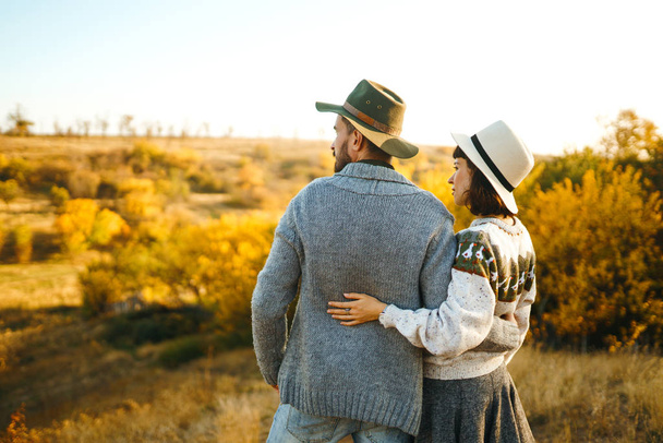Lovely hipster couple looking at each other. Couple wearing beautiful hats and sweaters. Lifestyle, happy couple of two play on a sunny day in the park. The concept of youth, love and lifestyle. Sunset in autumn  - Fotó, kép