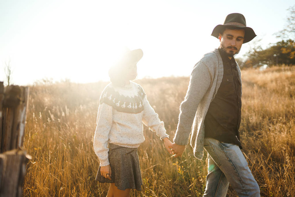 Lovely hipster couple looking at each other. Couple wearing beautiful hats and sweaters. Lifestyle, happy couple of two play on a sunny day in the park. The concept of youth, love and lifestyle. Sunset in autumn  - Φωτογραφία, εικόνα