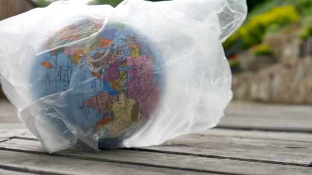 Side view of the Earth in polyethylene disposable package on wooden background. Concept of ecological problems. Stop garbage pollution - Кадры, видео