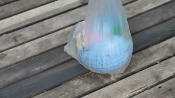 Dia Mundial do Ambiente. Alguém segura a terra num saco de plástico. O globo com nomes geográficos em letras cirílicas ucranianas sobre ele em polietileno pacote descartável em fundo de madeira
. - Filmagem, Vídeo