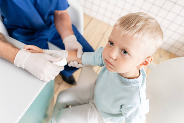 Doctor in blue uniform make elastic bandaged around a boy hand with trauma in his arm. in the hospital - Zdjęcie, obraz