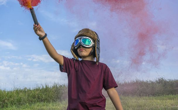 Little boy plays with colored smoke, wearing a 1920s aviator hat and airplane pilot glasses - Photo, image