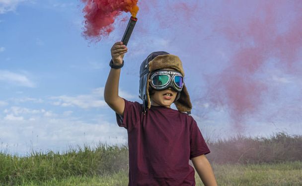 Little boy plays with colored smoke, wearing a 1920s aviator hat and airplane pilot glasses - Φωτογραφία, εικόνα