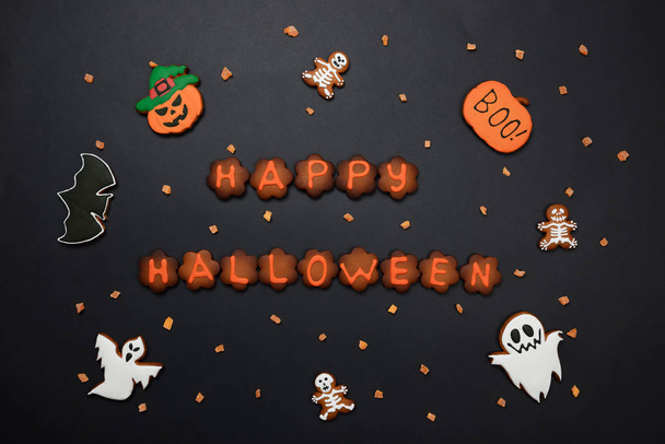 The hand-made eatable gingerbread Halloween inscription, pumpkin, ghosts, bat and sceletons on black background - 写真・画像