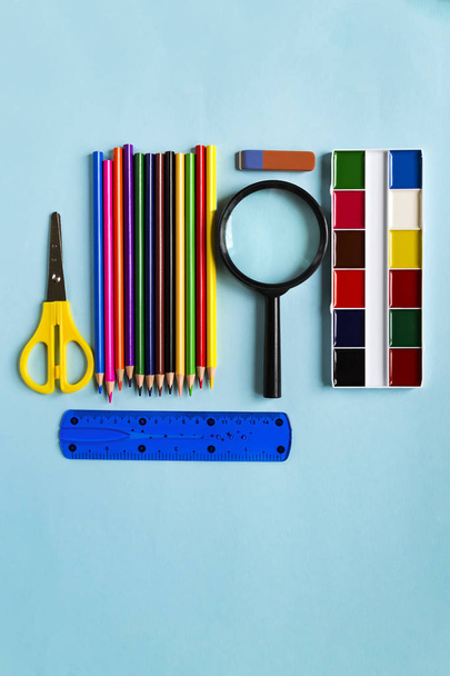 Een set van schoolbenodigdheden. Vergrootglas, potloden, liniaal, schede, aquarel op een blauwe papier achtergrond met ruimte voor tekst. Platte lay - Foto, afbeelding