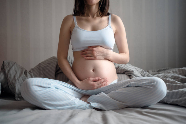 Крупный план беременной женщины, держащей живот руками над и снизу, медитация
 - Фото, изображение
