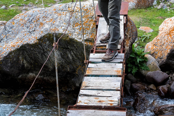 Beine des Wanderers auf schmaler Holzbrücke über Gebirgsfluss - Foto, Bild