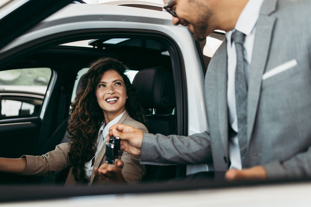 Happy and beautiful middle age business woman buying new car at showroom. A nice seller helps her make the right decision. - Foto, imagen
