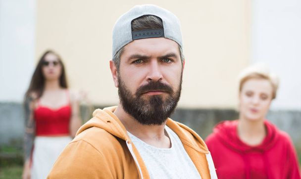 Cool hipster. Bearded man in fashion hipster cap outdoor. Brutal man with long beard and mustache. Hipster street fashion. Attractive guy in front of girl. Confident with his hipster style - Foto, Imagen