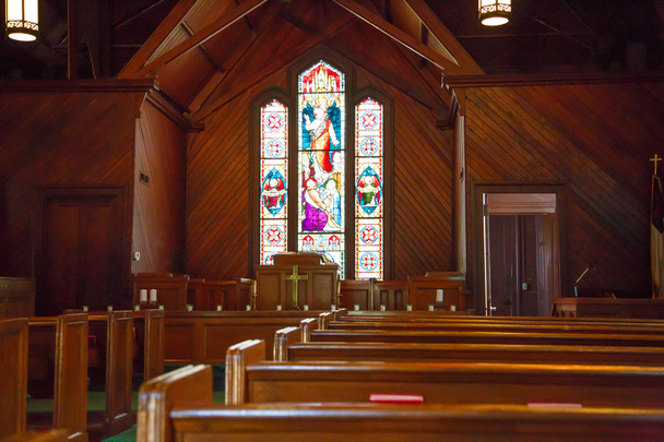 Pews de madeira e vidro manchado em pequena igreja
 - Foto, Imagem