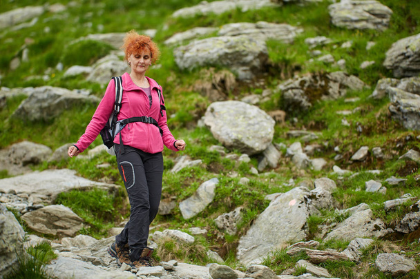 Woman with backpack hiking on trail in rocky mountains - Φωτογραφία, εικόνα