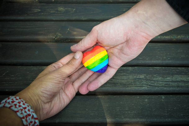 男性の手に虹のストライプと装飾的なハート。LGBTプライドフラグ、レズビアン、ゲイ、バイセクシャル、社会運動のためのトランスジェンダーのシンボル。同性愛、人権の概念。スペースのコピー. - 写真・画像