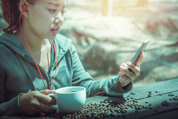Frauen trinken Kaffee spielen Handy auf dem Holztischboden liegt eine Kaffeebohne. - Foto, Bild