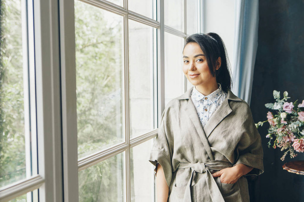 красива Азіатська жінка з зачіскою в японському стилі і кімоно біля вікна на тлі домашнього інтер'єру - Фото, зображення