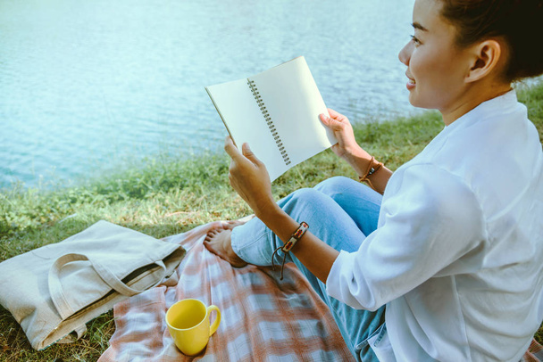 asiatische Frau sitzt entspannt im Park. Lesen und Kaffee trinken im Urlaub. - Foto, Bild