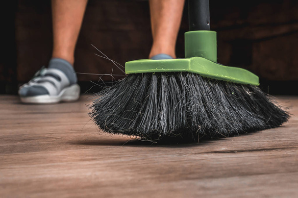 Woman with broom sweeping wooden laminate floor - Foto, Bild
