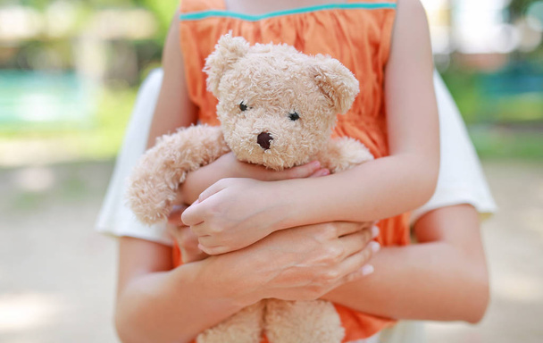Close-up hands of little child girl and mom hugging teddy bear. Mother and daughter cuddle doll. - Valokuva, kuva