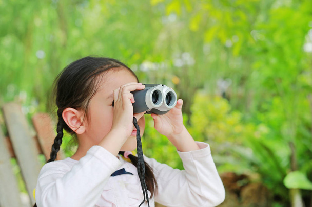 Little child girl in a field looking through binoculars in nature outdoor. Explore and adventure concept. - Foto, Imagem