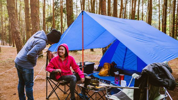 若いアジアのカップルが松の森でキャンプを楽しんでいます自然の中でキャンプページで座って食べ物を食べる. - 写真・画像