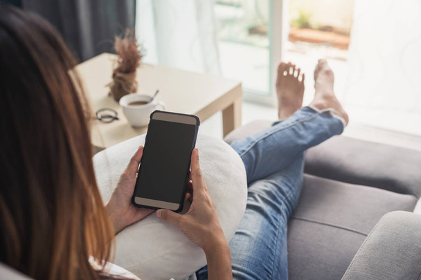 Young woman using smartphone at cozy home on sofa in living room - Fotó, kép