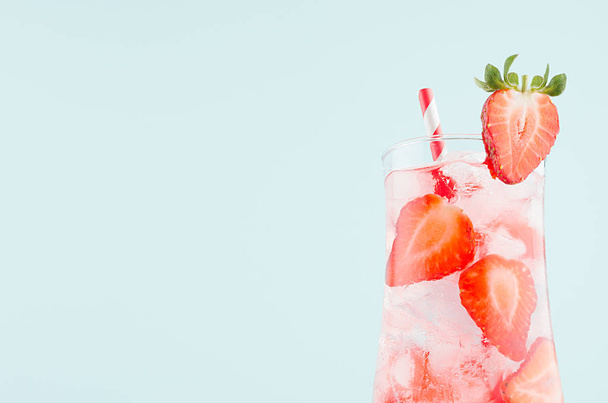 Fresh summer strawberry lemonade with ripe berry pieces, ice cubes, tonic, straw on light soft pastel blue color background, closeup, top, half, details.  - Photo, image