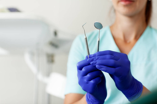 Nő fogorvos derzhit szakmai fogorvos eszközök a fogorvosi rendelő, tükör és ívelt csipeszek, kép a higiénia és a fogászati egészség - Fotó, kép