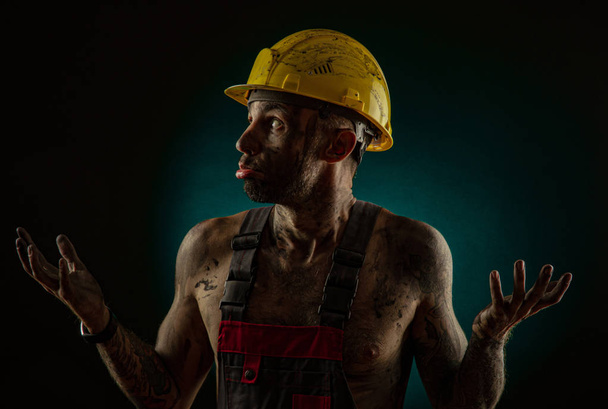 Un uomo minatore in abiti da operaio e un casco, sporco, in fuliggine, con un corpo nudo, smorfie alla telecamera
 - Foto, immagini