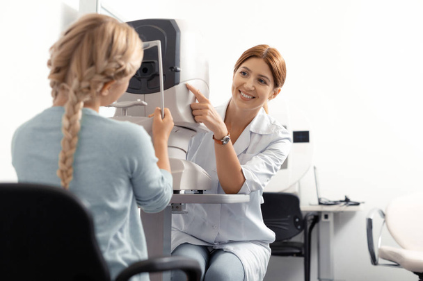 Eye doctor smiling while checking eye sight of teenage girl - Photo, image