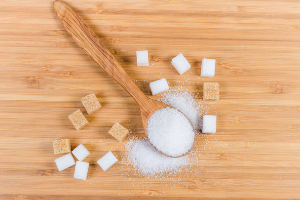White sugar in wooden spoon, white and brown sugar cubes - Photo, Image