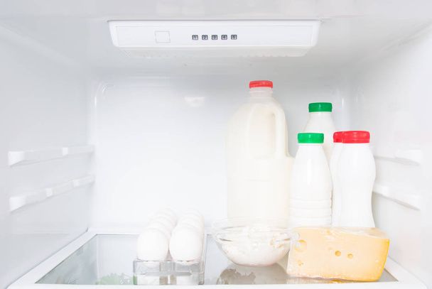 on a shelf in a white fridge, animal products, cream, milk, kefir, eggs, cottage cheese and cheese - Фото, изображение