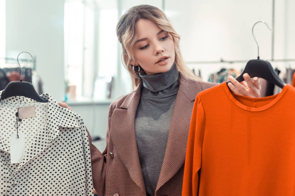Blonde woman looking at bright orange dress while shopping - Фото, зображення