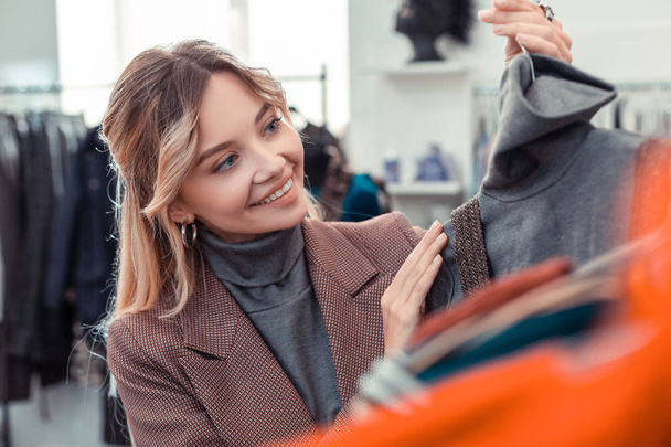 Blonde appealing woman smiling while choosing new outfit - Fotoğraf, Görsel