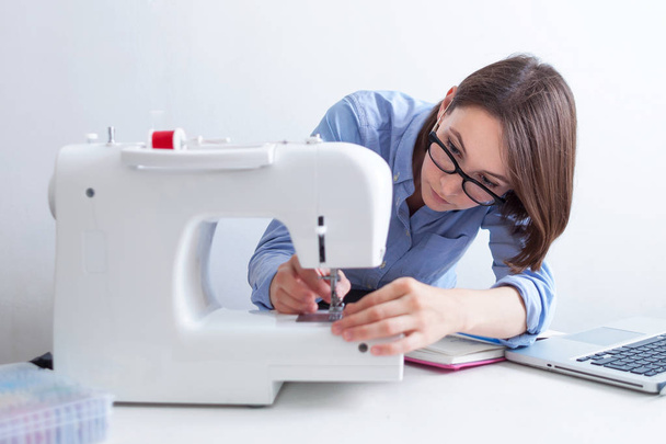 Seamstress sitting at desktop with garment equipments and analyzing information from laptop computer - Φωτογραφία, εικόνα