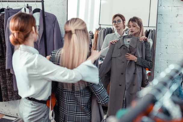 Woman speaking with shopping assistant while choosing coat - Foto, afbeelding