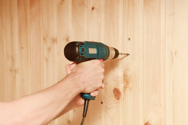Τρυπάνι στα χέρια ενός εργάτη γεώτρηση ένα ξύλινο τοίχο - Φωτογραφία, εικόνα