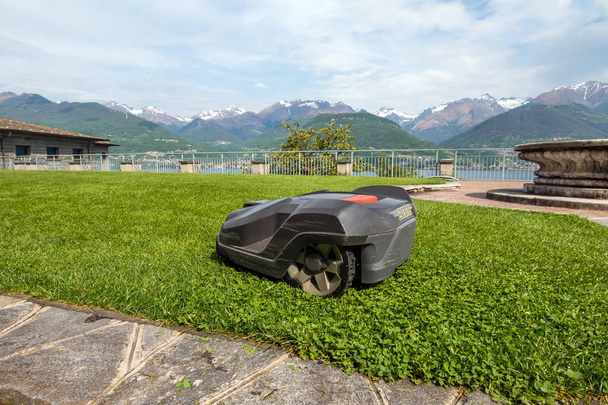 una cortadora de césped robótica que trabaja en un campo de hierba verde cerca del lago Como. Italia
 - Foto, imagen