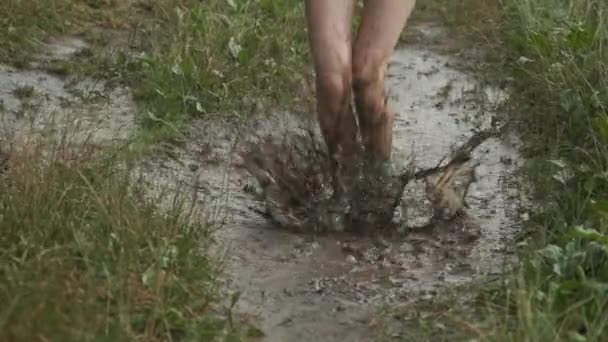 Close-up of girl legs in boots jumping in very muddy puddle - Materiał filmowy, wideo
