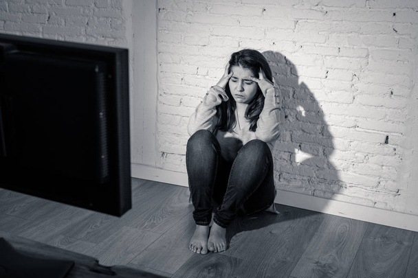 Dramatic portrait of intimidated young woman sitting on ground holding her head staring a computer suffering harassment. Being online abused by stalker feeling desperate in Internet problem concept. - Foto, Imagem