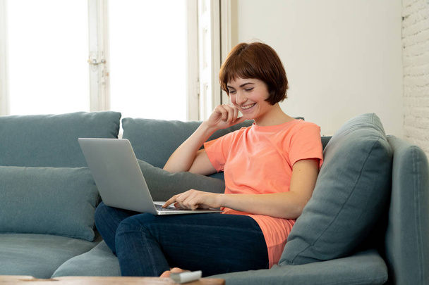 Lifestyle portrait of young attractive and relaxed woman using computer, enjoying watching online movie, working or studying at home smiling happy on the couch. In internet and social network concept. - Фото, зображення