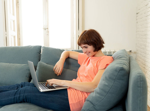 Lifestyle portrait of young attractive and relaxed woman using computer, enjoying watching online movie, working or studying at home smiling happy on the couch. In internet and social network concept. - Foto, Imagem