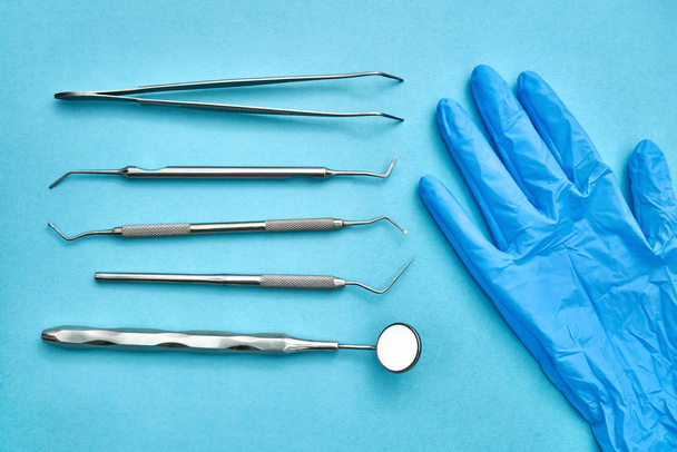 Dental instruments and protective glove lying on blue surface - Foto, Imagen