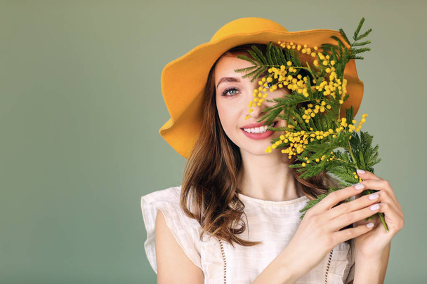 Beautiful young woman with bouquet of mimosa flowers on color background - 写真・画像